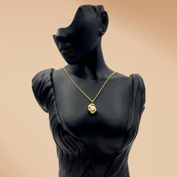 Black mannequin wearing a gold necklace on a beige background
