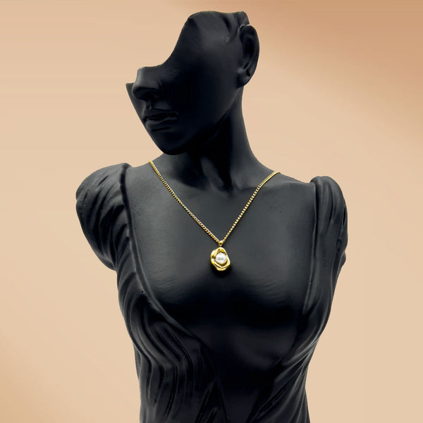 Black mannequin wearing a gold necklace on a beige background