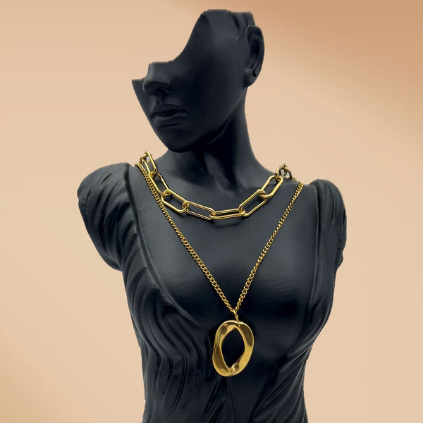 Black mannequin wearing a gold chain necklace with a beige background