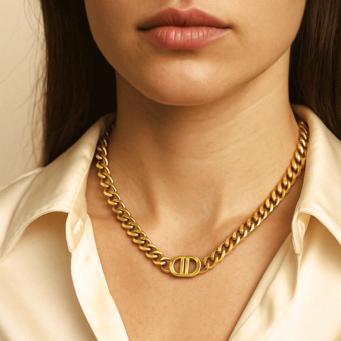 Gold chain necklace with a logo worn by a person against a neutral background